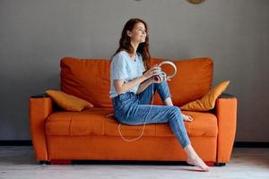 retrato de un mujer sentado en el sofá a hogar escuchando a música en auriculares tecnologías foto