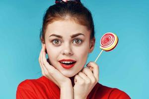 cheerful woman in a red t-shirt holding a lollipop blue background photo