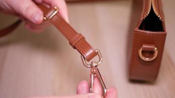 Women's hands demonstrate a belt with a carabiner for a women's bag video