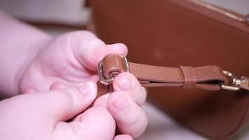 Women's hands demonstrate a belt with a carabiner for a women's bag video