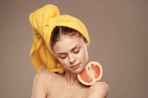 woman with bare shoulders yellow towel on her head grapefruit in hands clean skin care photo
