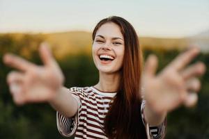 Woman smiling while looking at the camera and pulling her hands to the camera close-up in nature with a view of the mountains. Happy travel lifestyle follow me photo