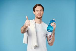 sporty man showing thumb up water bottle towel on shoulder cropped view blue background photo