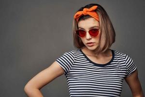 mujer vistiendo Gafas de sol en un a rayas camiseta con un vendaje en su cabeza posando Moda foto