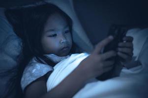 Asian kid playing game on smartphone in the bed at night,The girl Addict social media photo