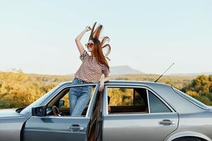 Happy woman traveler climbed on the car and spread her arms smiling happily. looks at the nature around. Lifestyle in travel and joy photo