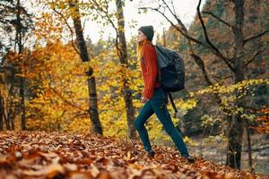 woman traveler with backpack walking in the park in autumn in nature side view photo