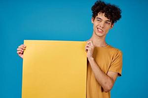 emotional man with curly hair yellow poster in the hands of copy space photo