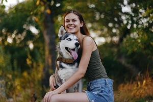 Joyful woman with a husky breed dog smiling while sitting in nature on a walk with a dog on a leash autumn landscape on the background photo