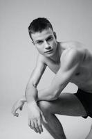 athlete with a pumped-up torso leaning on his knee portrait cropped black and white photography model photo