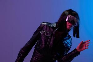Confused adorable brunet woman in leather jacket specular sunglasses open mouth look aside posing isolated in blue violet color light background. Neon party Cyberpunk concept. Copy space. Good offer photo