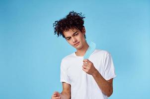 brunette guy with curly hair on a blue background and a comb in his hand photo