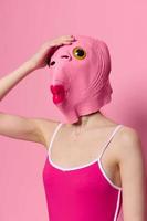 Woman with fish head mask on pink is holding her head in surprise, modern art photo on pink background