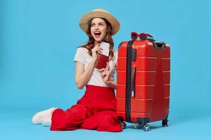 woman with red suitcase sitting on the floor of passport plane tickets travel blue background photo