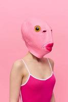 Funny crazy woman on a pink background standing in a fish head mask on a pink background, conceptual Halloween costume art photo