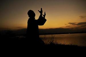 silueta joven asiático musulmán hombre Orando en puesta de sol, ramadán festival concepto foto