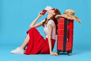 woman with red suitcase sitting on the floor of passport plane tickets travel blue background photo