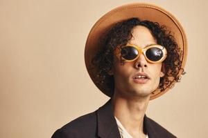 linda increíble bronceado Rizado hombre en clásico sombrero marrón chaqueta de moda Gafas de sol posando aislado en beige pastel antecedentes. Moda nuevo colección oferta. retro estilo retrato concepto. gratis sitio para anuncio foto