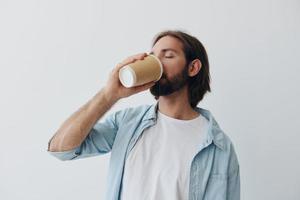 Lanza libre milenario hombre con barba Bebiendo café desde un cangrejo taza en elegante hipster ropa en un blanco antecedentes foto