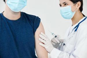 hermosa enfermero en un médico máscara dando un inyección a un paciente en un azul camiseta codicioso foto