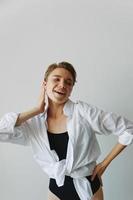 Young woman teenager listening to music with infertile headphones and dancing home, grinning with teeth with a short haircut in a white shirt on a white background. Girl natural poses with no filters photo