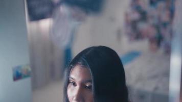 ett asiatisk tonåring utseende i de spegel med en känsla av osäkerhet eftersom henne ansikte video