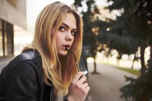 Happy blonde woman in leather jacket trendy glasses nature park street photo