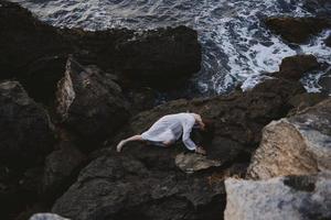 Barefoot woman in long white dress wet hair lying on a rocky cliff landscape photo