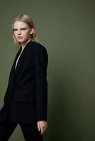 A bright expressive strict girl professional model walks to the side in motion looks at you in the camera posing on a green olive background in the studio photo