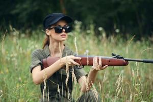 Woman on outdoor in dark glasses with weapons shelter hunting green leaves green trees photo