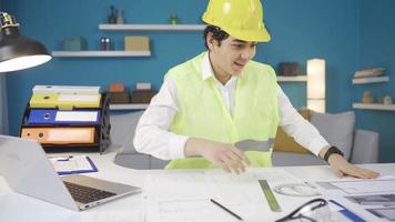 Funny boy working at his desk wearing engineering clothes and hard hat. The dreamer boy dreams of becoming an Engineer in the future, He looks at the project drawings. video