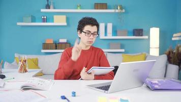 masculino estudiante estudiando remotamente en línea. un masculino estudiante asistiendo un en línea lección desde hogar pregunta su profesor un pregunta. video