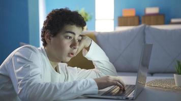 adolescente masculino usando computador portátil dentro uma entediado e depressivo estado. adolescente Garoto usando computador portátil sozinho às lar, entediado e depressivo. video