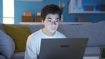 pojke ser på bärbar dator allvarlig och fokuserad, misstänkt närma sig. pojke ser på bärbar dator misstänkt och fokuserad. allvarlig pojke använder sig av bärbar dator på natt. video