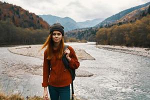 beautiful woman in a sweater with a backpack in the mountains near the river in nature portrait photo