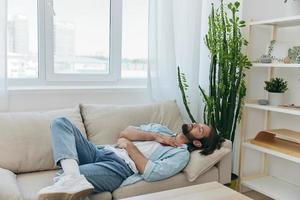 un hombre con un barba duerme en el sofá en el tarde cansado y relajado después estrés y enfermo salud. estrés a trabajar, pobre dormir y salud problemas foto