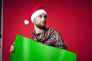 handsome man in a santa hat holding a banner holiday red background photo