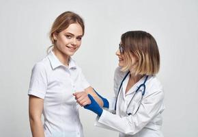 hembra médico en un médico vestido y azul guantes examina un paciente en un recortado ver foto