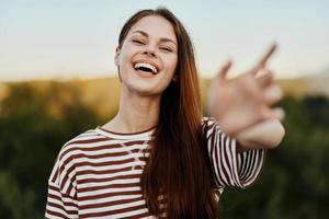 Woman smiling while looking at the camera and pulling her hands to the camera close-up in nature with a view of the mountains. Happy travel lifestyle follow me photo