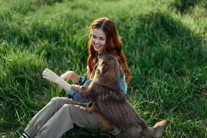 Woman lying on the grass smiling playing and cuddling her dog in nature in the park in the summer sunset. The concept of health and love of animals, treatment of ticks and fleas grass and animals photo