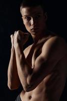 sporty guy with pumped up arm muscles on a black background looking to the side close-up portrait photo