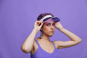 Portrait of a sporty fashion woman posing in a purple sports suit for yoga and a transparent cap on a purple background monochrome photo