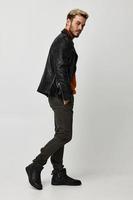 a man in a leather jacket, orange sweater and trousers turned to the side on a Light background copy Copy Space photo