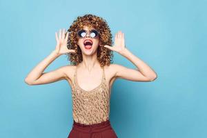 Charming model Curly hair emotions sunglasses hands near face blue background photo