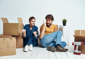 A man and a woman are sitting on the floor indoors near the couch and moving boxes photo