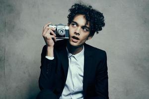 curly-haired man in a jacket and shirt holding a camera in his hand model vogue style photo