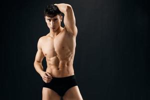 handsome male bodybuilder in black panties with a pumped-up body studio photo