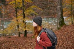 traveler with a backpack and in a gray hat in the autumn forest fallen leaves trees river model photo