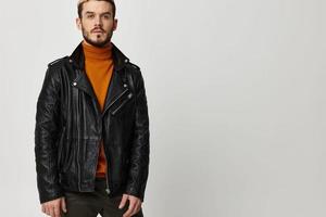 sexy young man in an orange sweater and in a leather jacket on a light background photo