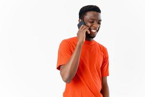 happy guy of african appearance talking on the phone on a light background and an orange t-shirt smile model photo